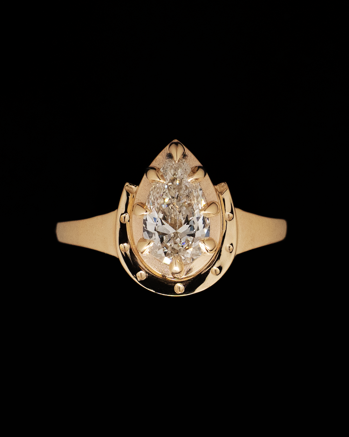 A pear-cut diamond set in a yellow gold horseshoe engagement ring, on a black background