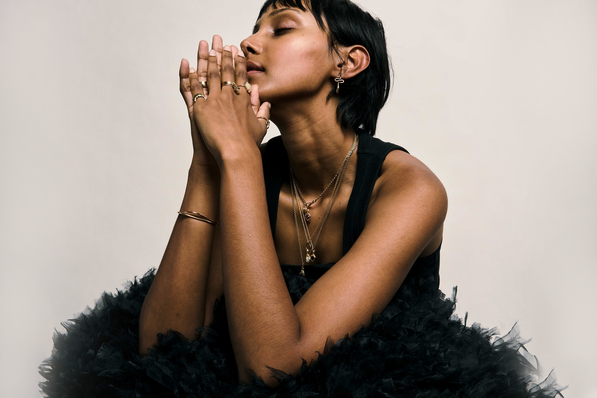 A model wearing a stack of solid 9ct gold rings, including a black heart signet and a red stone cluster, with a pearl earring