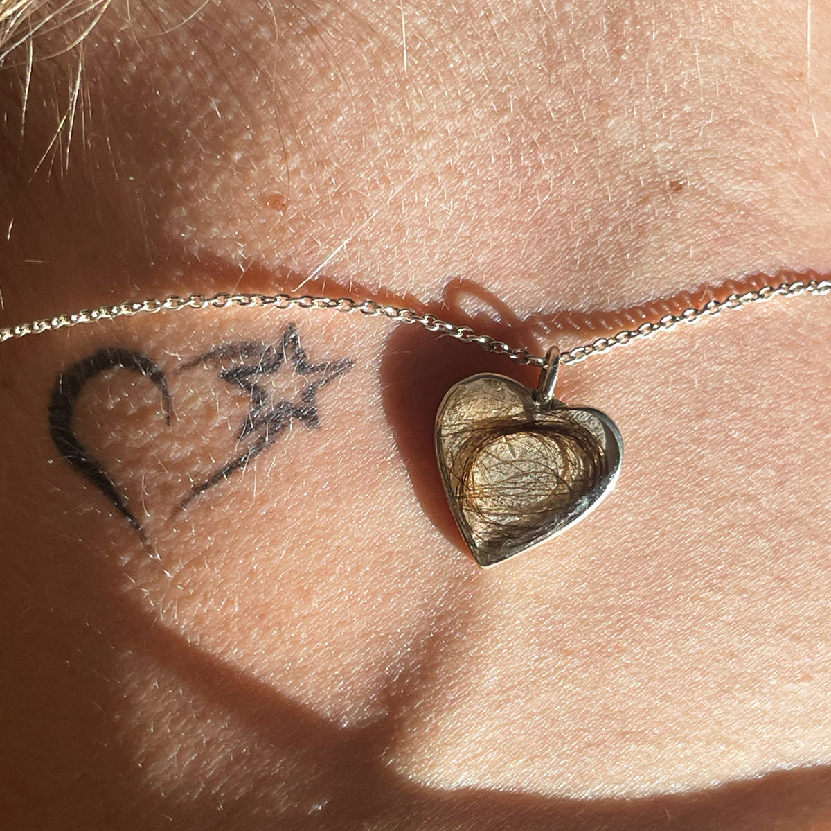A sterling silver heart pendant with a lock of hair sealed inside, worn on a fine chain