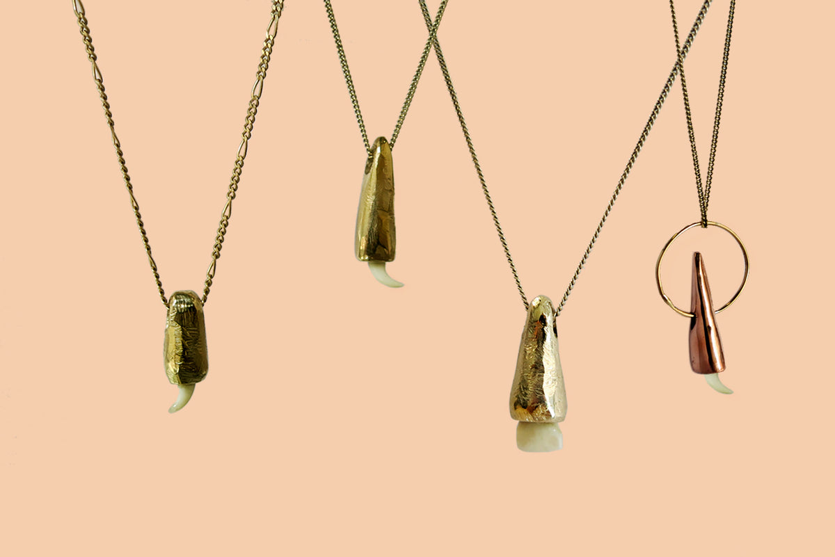 A dog's tooth capped in solid 9ct gold, hanging from a fine gold chain on a white background